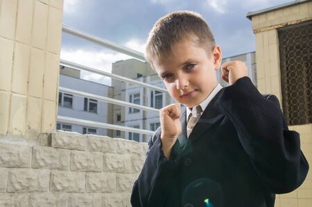 Little schooler Boxing is in front, raising his fists at school yard の写真素材