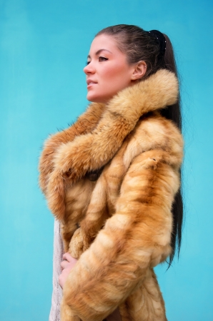 Beautiful woman in a fur coat against blue backgroundの写真素材