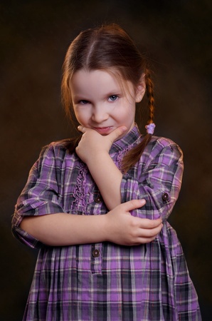 Little girl dressed in a plaid dress with crossed hands on the chest.の写真素材