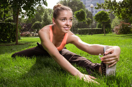 Beautiful young woman doing stretching exercise on green grass at park. Yoga