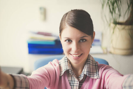 Portrait of young caucasian business woman in pink vest at her office doing selfie