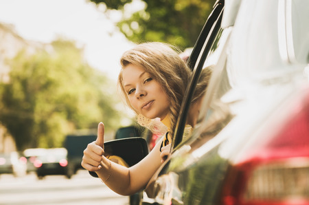 Beautiful caucasian young woman in car showing the thumb upの写真素材