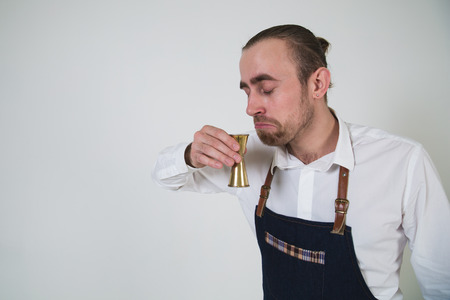 A shoot of young caucasian men in apron as a barmen drinking.