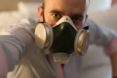 Handsome young stylish caucasian man in respirator on the bed in the bedroomの写真素材
