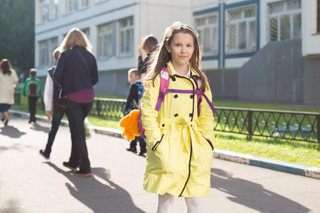 Attractive young caucasian schoolgirl in yellow coat going with backpackの写真素材