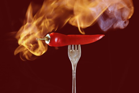 chili pepper red on fire on a dark red backgroundの写真素材