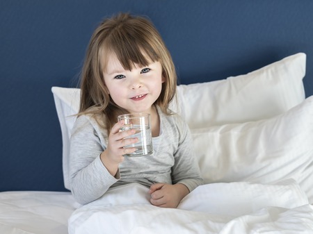 Little girl drinking water on white bedの写真素材