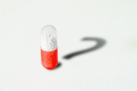 Pill and shadow in the form of a question mark on a white background. Healthcare concept.の写真素材