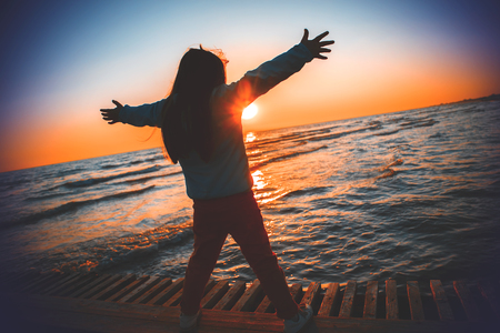 Silhouette girl raising hands on the beach in sunrise.の写真素材