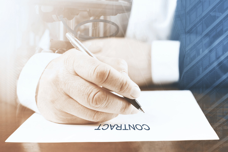Close up of businessman sitting at table and signing documentの写真素材