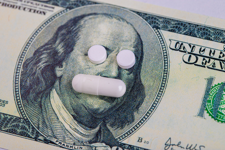 A pills lie in place of the eyes, on a bill of one hundred dollars close-up. The concept of insurance medecine, high cost, high cost of drugs. Costly treatment.の写真素材