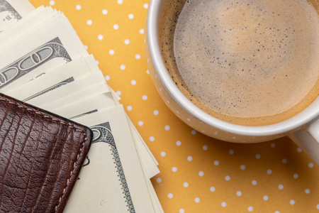 Top view of a cup of coffee and a stack of dollar bills in a purse.の写真素材