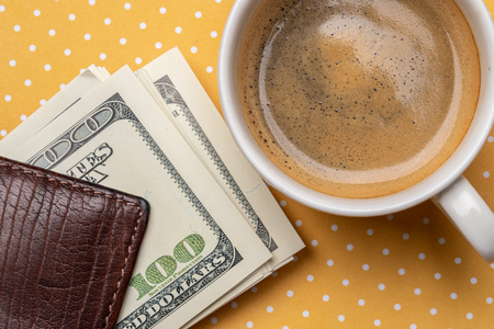 Top view of a cup of coffee and a stack of dollar bills in a purse.の写真素材