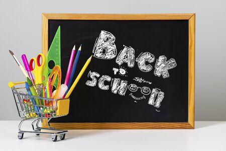Various colorful school supplies and shopping trolley on the background of the school board with the text back to schoolの写真素材
