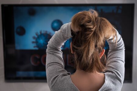 A woman watches a television program about the distribution of Ð¡OVID. The concept of a depressive state.の写真素材
