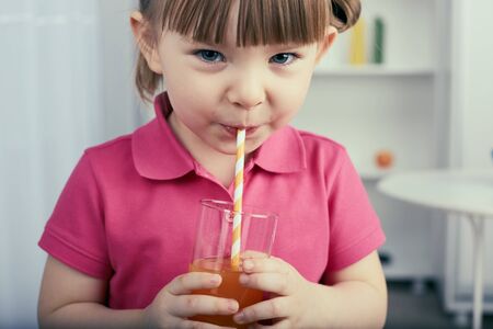 Cute little girl drinks orange juice at home.の写真素材