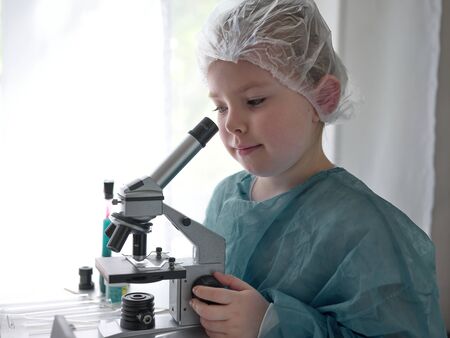 Cute little girl looking into microscope at his desk at home. Young scientist making experiments in his home laboratory. Education concept.の写真素材