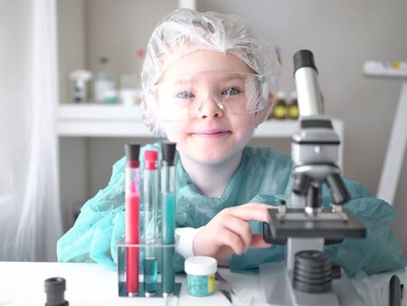 Cute little girl looking into microscope at his desk at home. Young scientist making experiments in his home laboratory. Education concept.の写真素材