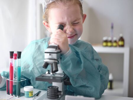 Cute little girl looking into microscope at his desk at home. Young scientist making experiments in his home laboratory. Education concept.の写真素材