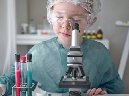 Cute little girl looking into microscope at his desk at home. Young scientist making experiments in his home laboratory. Education concept.の写真素材