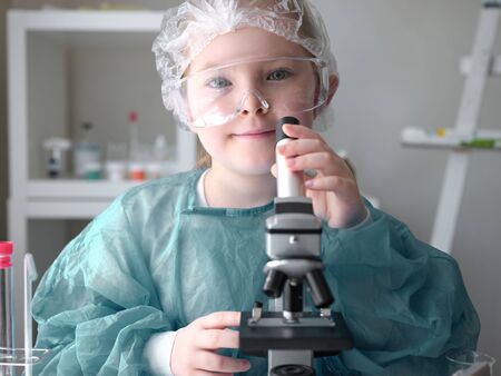 Cute little girl looking into microscope at his desk at home. Young scientist making experiments in his home laboratory. Education concept.の写真素材