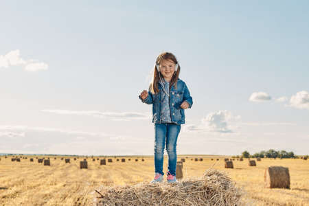 A cute little girl listens to music and dances on a haystack. High quality photoの写真素材
