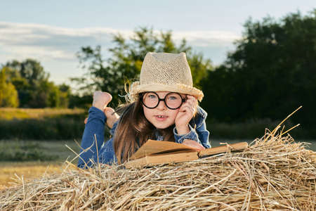 Reading girl sits over the haystack roll on field in countryside. High quality photoの写真素材