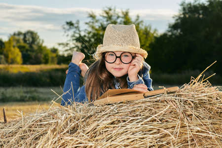 Reading girl sits over the haystack roll on field in countryside. High quality photoの写真素材