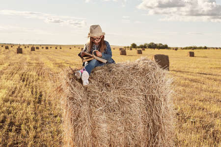 Reading girl sits over the haystack roll on field in countryside. High quality photoの写真素材