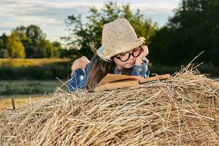 Reading girl sits over the haystack roll on field in countryside. High quality photoの写真素材