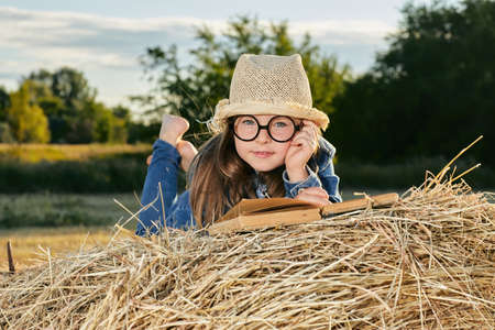 Reading girl sits over the haystack roll on field in countryside. High quality photo.の写真素材
