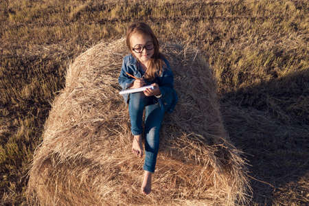 Aerial photo. A girl sits on a haystack and paints a landscape. View from above. Selected focusの写真素材