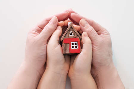 real estate and family home concept - closeup picture of child and female hands holding red paper house with family. High quality photoの写真素材