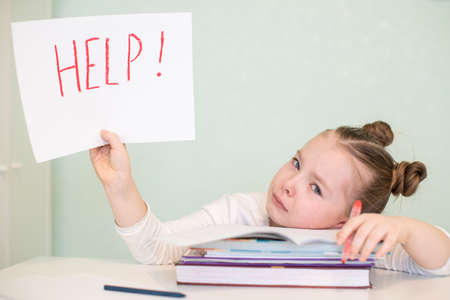 A little girl cries sitting at a table and she holds a hand paper with the inscription HELP. High quality photoの写真素材