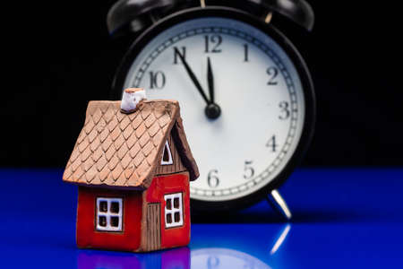 Model of cardboard house with alarm clock, real estate, cost of housing or buying a new home concept. High quality photoの写真素材