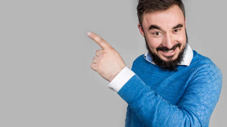 Smiling business man pointing left with index finger and looking at camera, isolated on gray background. High quality photoの写真素材