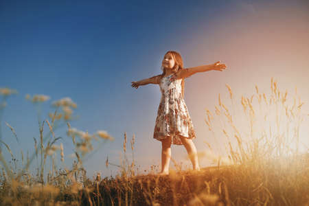A little girl in the field with her hands up in the air. High quality photoの写真素材