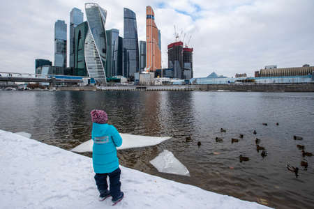Moscow, Russia - February 1, 2021: A girl feeds ducks on the Moscow River opposite Moscow City in downtown Moscow. High quality photoのeditorial素材