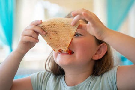 A young girl with plaits is eating a piece of pizza. High quality photoの写真素材