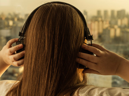 Girl in headphones looking at the city through the window, view from the back. High quality photo