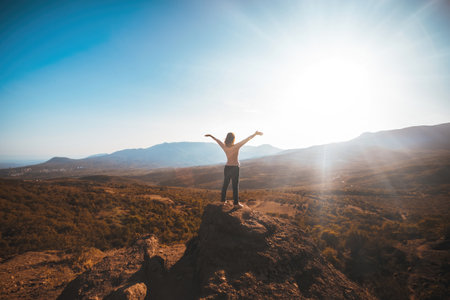 The girl looks at the mountains while facing the sun. High quality photo