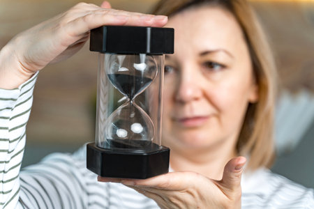 A woman holds an hourglass in front of her, looks at it. Concept of passing time. Selected Focus....