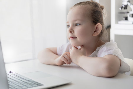 Cute little girl using laptop at home. Education, online study, home studying The girl at home...