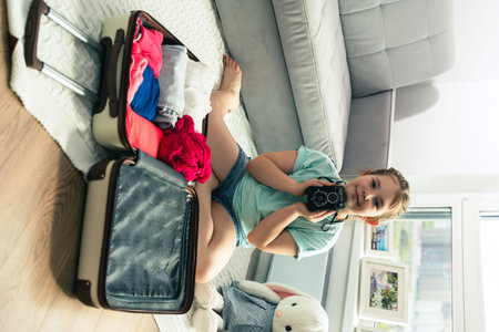 Happy little girl packing a suitcase for a trip. Cute girl traveler with retro camera getting ready for adventure. High quality photoの写真素材
