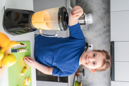 Pretty little girl making fruit puree in a blender at home in the kitchen. Selected focus. High quality photoの写真素材