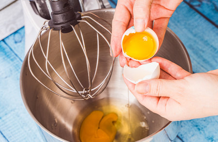 A woman's hands break an egg into the bowl of a mixer. Crepe suzette recipe. Close-up. Selected focus. High quality photoの写真素材