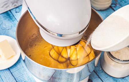 Sugar is poured into the bowl of a planetary mixer with beaten eggs. Recipe Crepe suzette. Selected focus. High quality photoの写真素材
