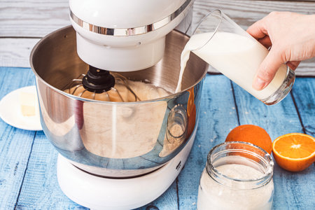 A woman's hand pours the milk into the bowl of the mixer, adding it to the beaten eggs. Crepe suzette recipe. Selected focus. High quality photoの写真素材