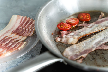 Close-up of sauteed bacon and tomatoes in a pan next to a plate of bacon. Delicious breakfast. Selected focus. High quality photoの写真素材