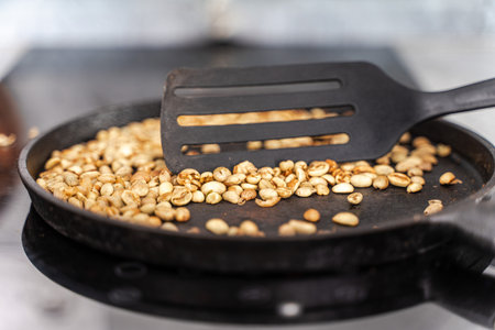 Coffee beans are roasted in a cast-iron pan. Green grains are mixed with a spatula. Selected focus. High quality photoの写真素材